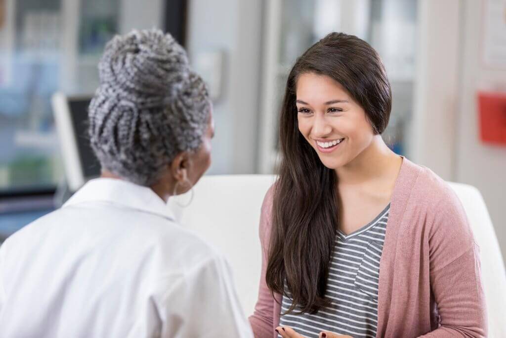 teenage girl smiling as she talks with a female doctor